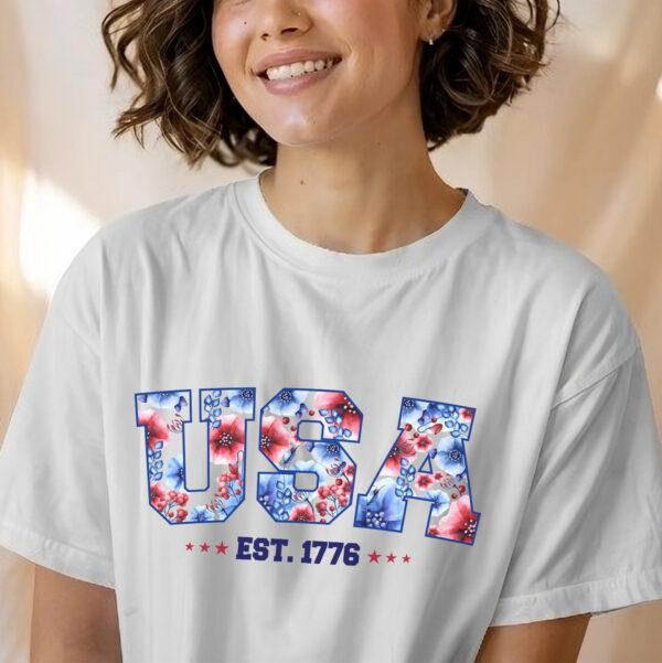 Women wearing a white shirt with text "USA" red and blue floral "est 1776" design